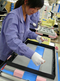 The next worker prepares the front bezel and adds cushioning material before placing the LCD panel inside.